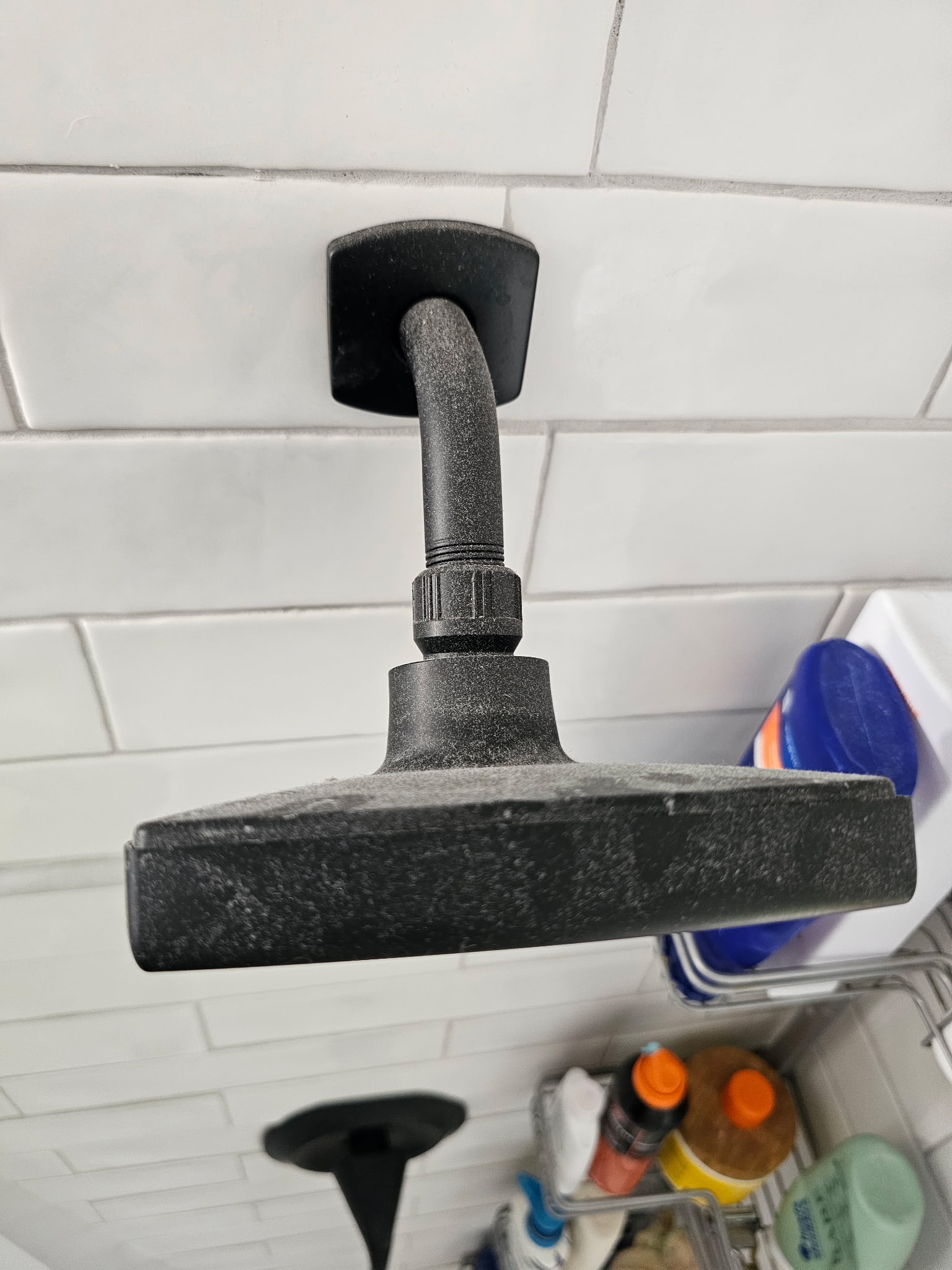 Matte black rain shower head coated with heavy hard water minerals and chalky scale before cleaning